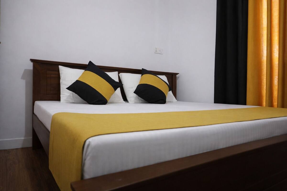 Una cama con cabecera de madera, ropa de cama blanca y dos almohadas negras y amarillas.