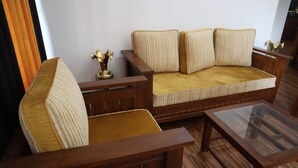 Un canapé en bois avec un siège et un dossier rembourrés, une table basse avec un plateau en verre et un petit objet décoratif posé sur une table d’appoint en bois.