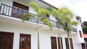 Un immeuble de deux étages doté d’un balcon, de volets en bois et de plantes en pot.
