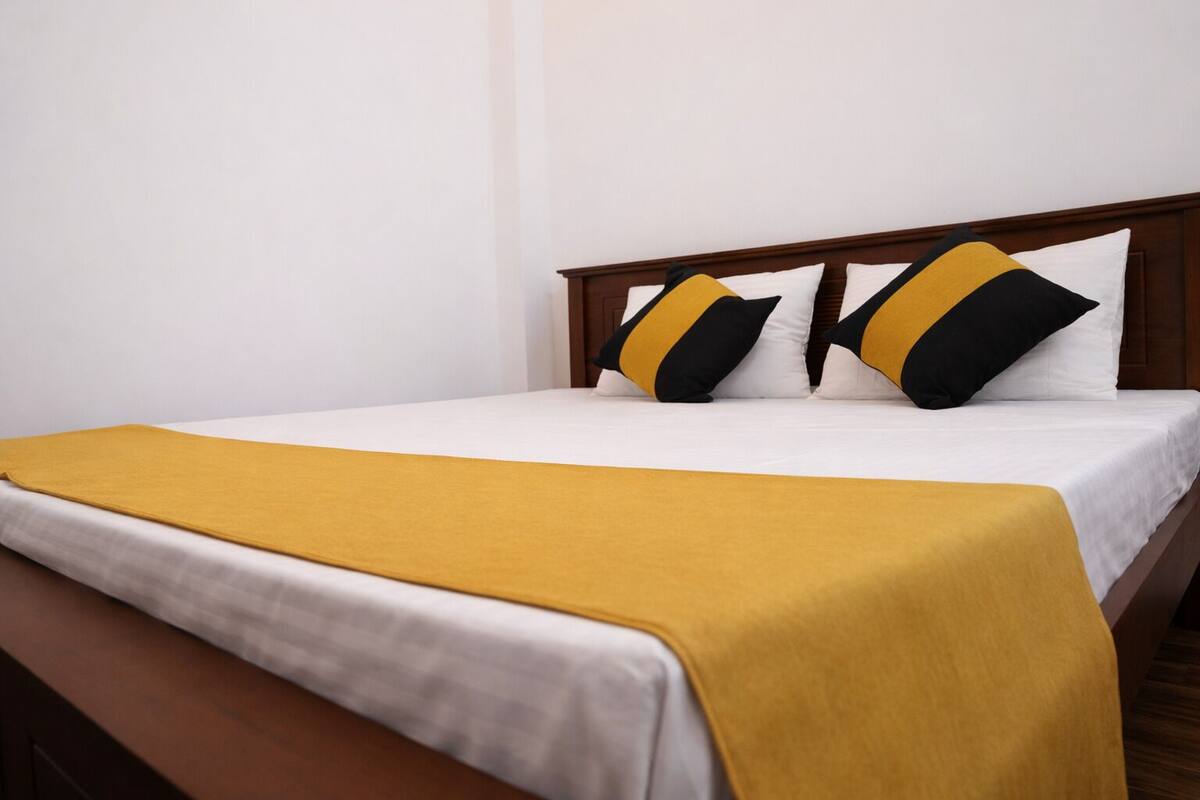 Una cama bien hecha con sábana blanca y manta color mostaza.