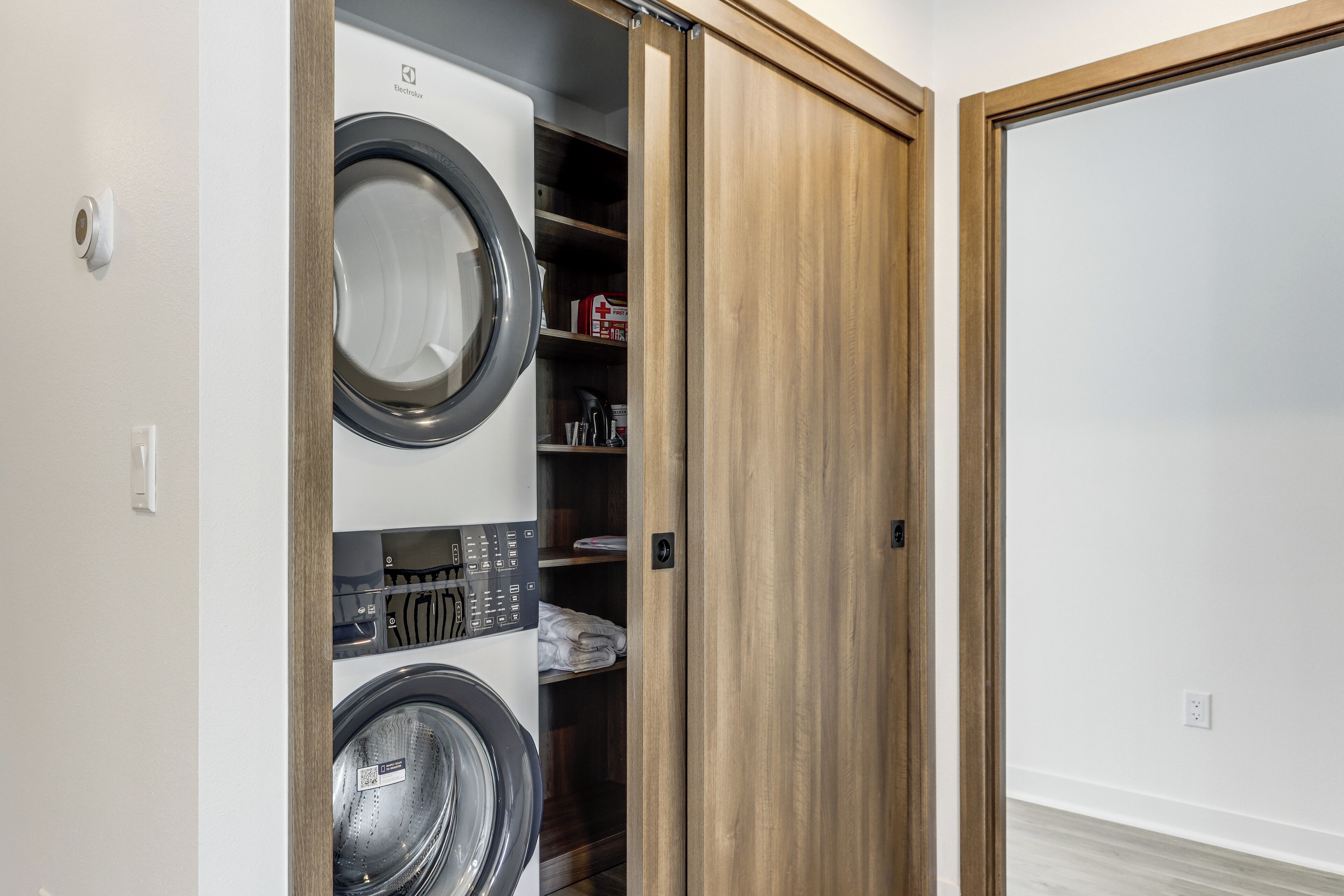 A laundry room with a front-loading washer and dryer, wooden shelving, and a closed door.