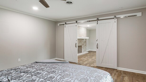 Un dormitorio con cama, ventilador de techo, armario con puerta corredera y suelo de madera.