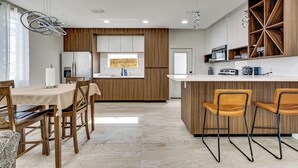 A modern kitchen with a central island, wooden cabinetry, and a dining area with a table and chairs.