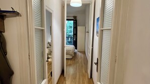 Um corredor estreito com piso de madeira, paredes brancas e um lustre.