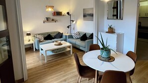 Uma sala moderna com sofá, mesa de centro, mesa de jantar e cadeiras. Uma área de cozinha é visível ao fundo.