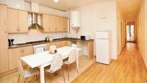 Uma cozinha moderna com armários de madeira, bancada branca e um espaço de refeições com mesa e cadeiras brancas.