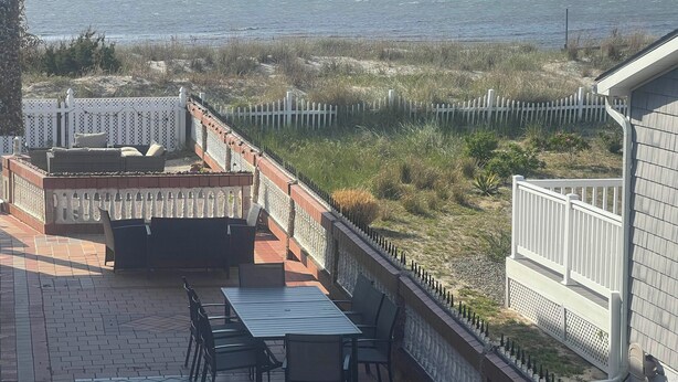 Un patio con una mesa y sillas, un rincón de estar con cojines y vista a la playa.