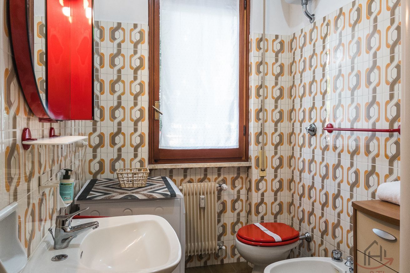 Ein Badezimmer mit einem weißen Waschbecken, einer roten Toilette, einem Spiegel und Wandtapete mit Muster.