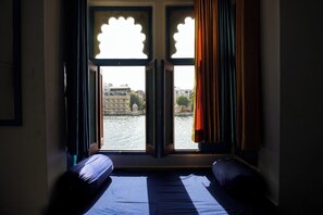 Una stanza con un letto, una finestra con tende e vista su un fiume e degli edifici.