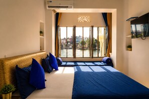 Una habitación de hotel con un ventanal grande, una cama con ropa de cama azul y un cabecero dorado.