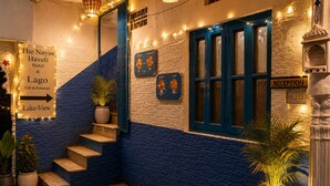 A hotel entrance with a staircase leading to the upper floor, a reception desk, and a sign for The Nayee Haveli Hotel & Lago Café & Restaurant.