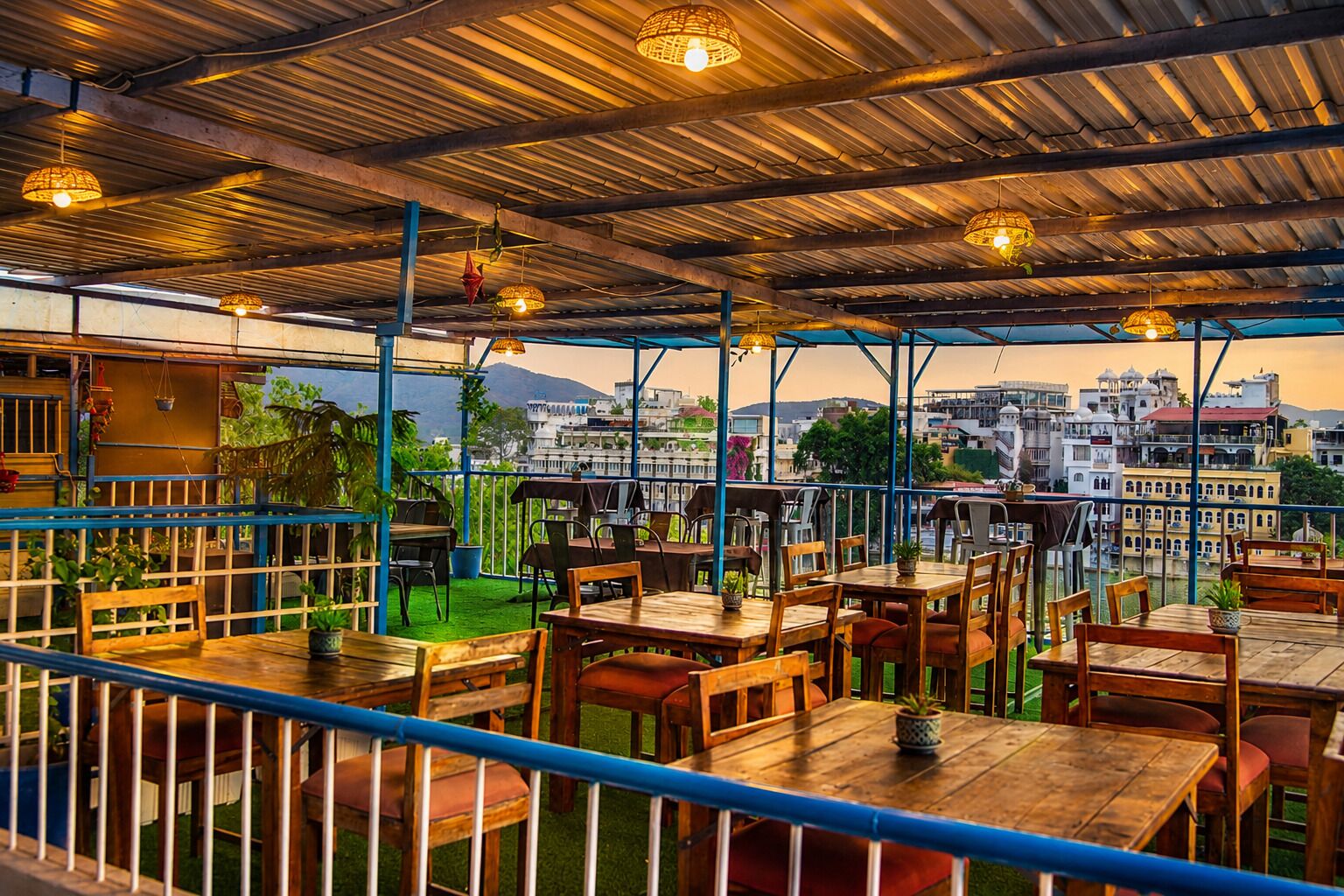 An outdoor restaurant with tables and chairs, a view of buildings in the background, and a covered area with a metal roof.