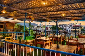 An outdoor restaurant with tables and chairs, a view of buildings in the background, and a covered area with a metal roof. - Hotel The Nayee Haveli - Lake View Hotel (Udaipur)