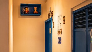 A narrow hallway with a blue door, a hanging light fixture, and a small shelf with decorative items.