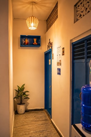 Un pasillo estrecho con una puerta azul, una lámpara colgante y un estante con adornos.