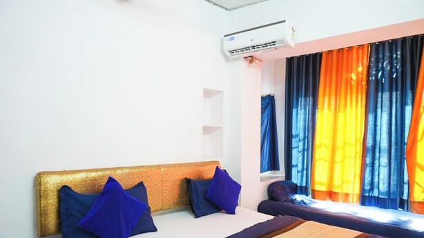 A hotel room with a bed, pillows, a window with curtains, and an air conditioning unit.