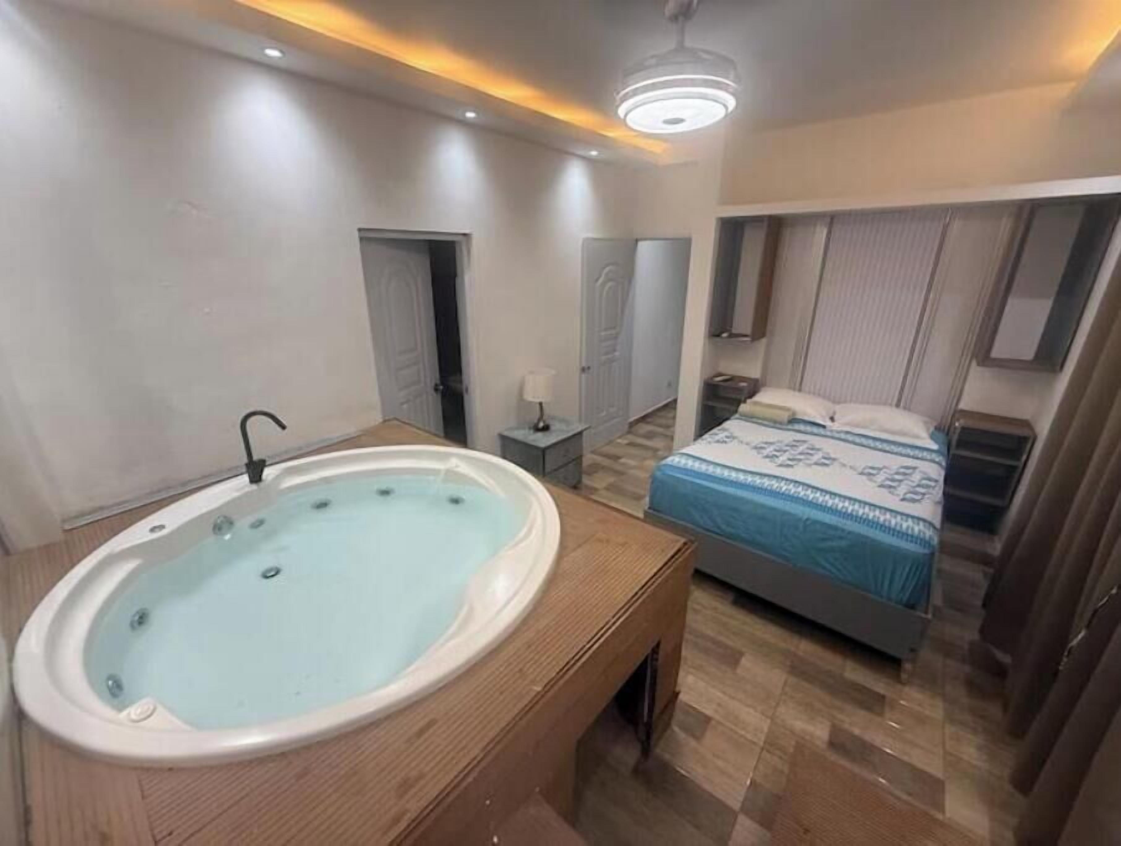 Un dormitorio con bañera, cama, mesita de noche y luz en el techo.