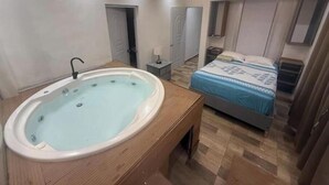 Un dormitorio con bañera, cama, mesita de noche y luz en el techo.