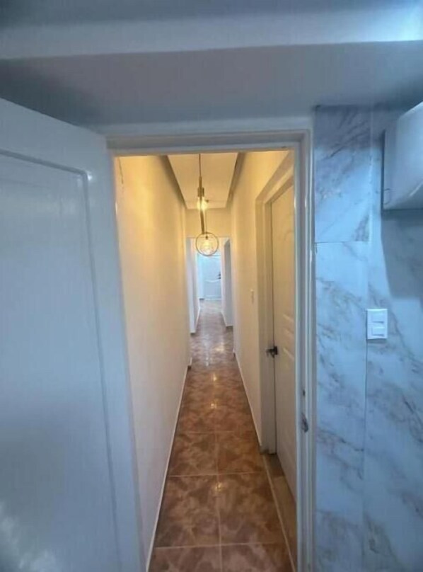 Un couloir avec un mur en marbre, un luminaire et une porte au fond.