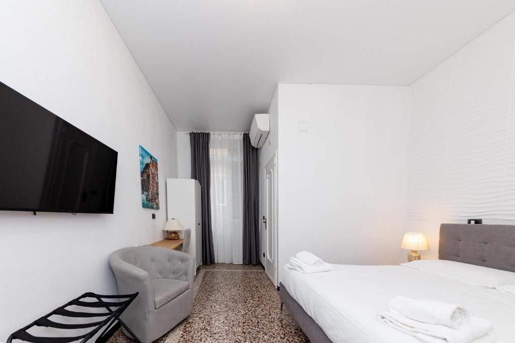 Une chambre d’hôtel avec un lit, un téléviseur fixé au mur, une chaise, un bureau avec une lampe et une fenêtre avec des rideaux.