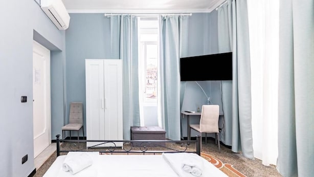 A hotel room with a bed, two chairs, a desk, a TV, and an air conditioning unit. - GALIA ROOMS (Genoa)