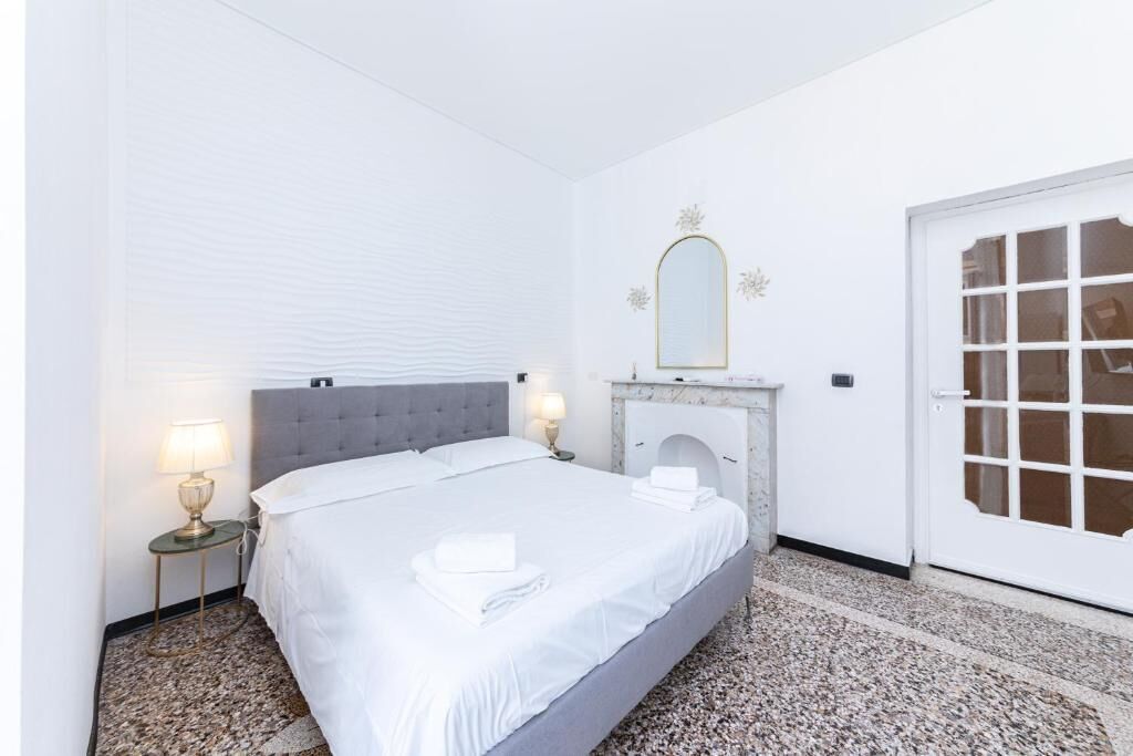 Ein Schlafzimmer mit Bett, Nachttischlampen, einem Spiegel, einem Kamin und einer Tür.