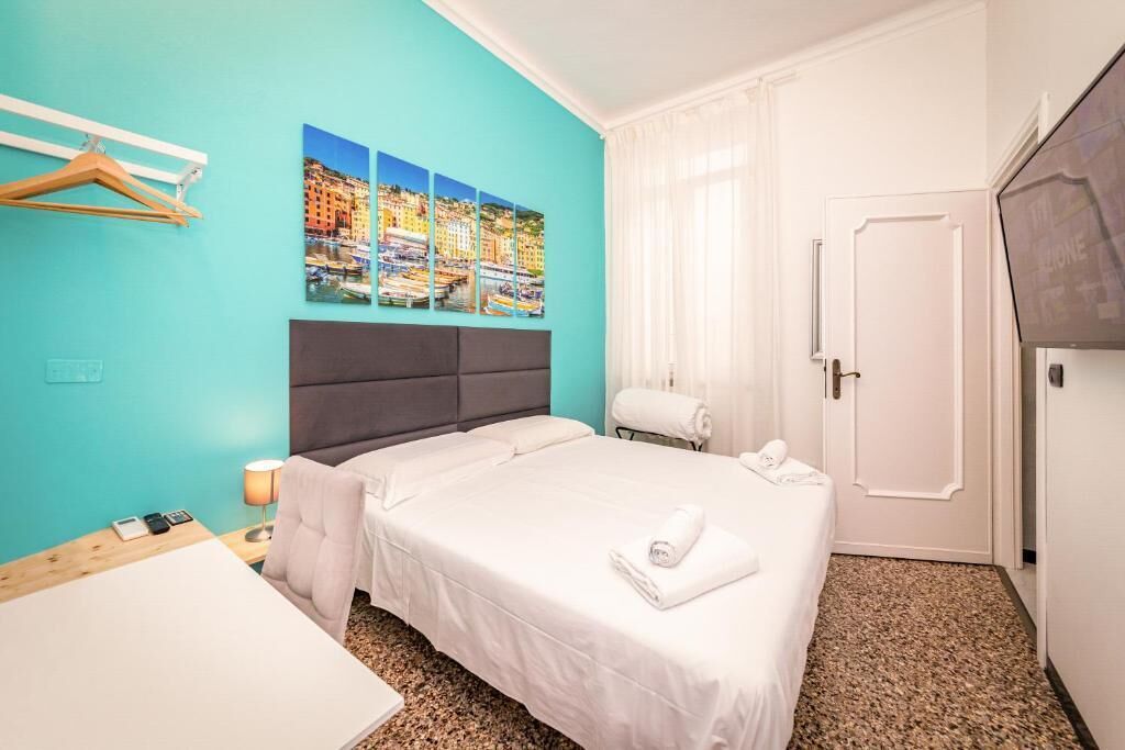 A hotel room with a bed, a desk, a chair, a hanging coat rack, a bathroom with a towel rack, and a door.