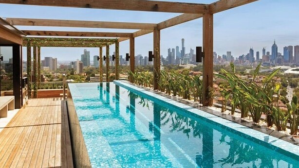 Una piscina en la azotea con vistas a un horizonte urbano, pérgola de madera y plantas en macetas.