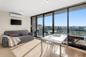 Ein modernes Wohnzimmer mit einem grauen Sofa, einem Glastisch und einem großen Fenster mit Blick auf die Stadt.