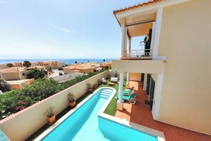 A swimming pool with a view of the sea, a covered patio with lounge chairs, and a building with a balcony. - Villa with stunning Ocean Views & Priv. Heated Pool (Luz)