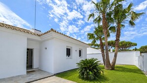 A white building with a tiled roof, a small front yard with grass and a palm tree, and a clear blue sky. - 4 bedroom lovely home in Roche (Roche)