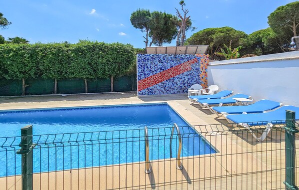 Une piscine avec un mur carrelé, des chaises longues et une clôture.