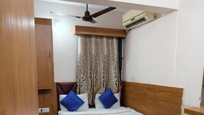 Ein gemütlicher Raum mit einem Bett, einem Deckenventilator, einer Klimaanlage und einem gemusterten Vorhang.