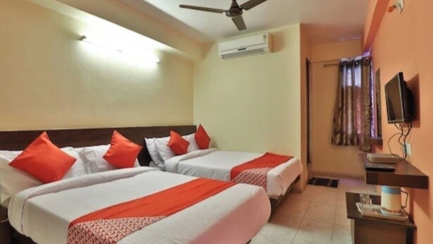 Ein Hotelzimmer mit zwei Betten, einem Deckenventilator, einer Klimaanlage, einem Fernseher und einem kleinen Tisch mit einer Lampe.