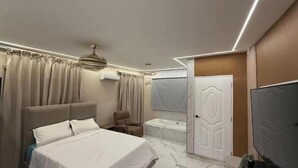 A modern bedroom with a bed, a chair, a TV, a bathtub, and a door. - Paradise paradise oasis private jacuzzi (Santo Domingo)