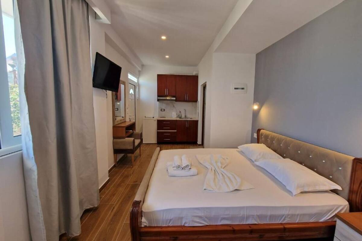 A hotel room with a bed, a TV, a kitchenette, and a window with curtains.