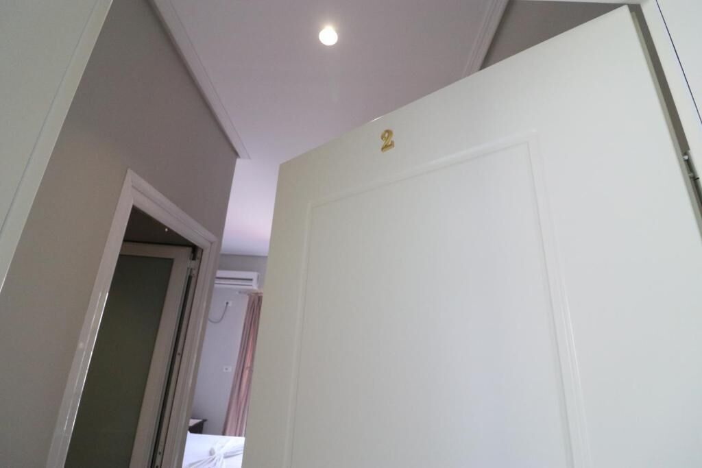 Un corridoio con una porta bianca numerata 2, una lampada a soffitto e un bagno parzialmente visibile con una doccia.