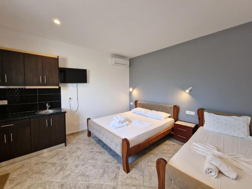 Ein Hotelzimmer mit Bett, Nachttisch, Wandfernseher und integrierter Küchenzeile.