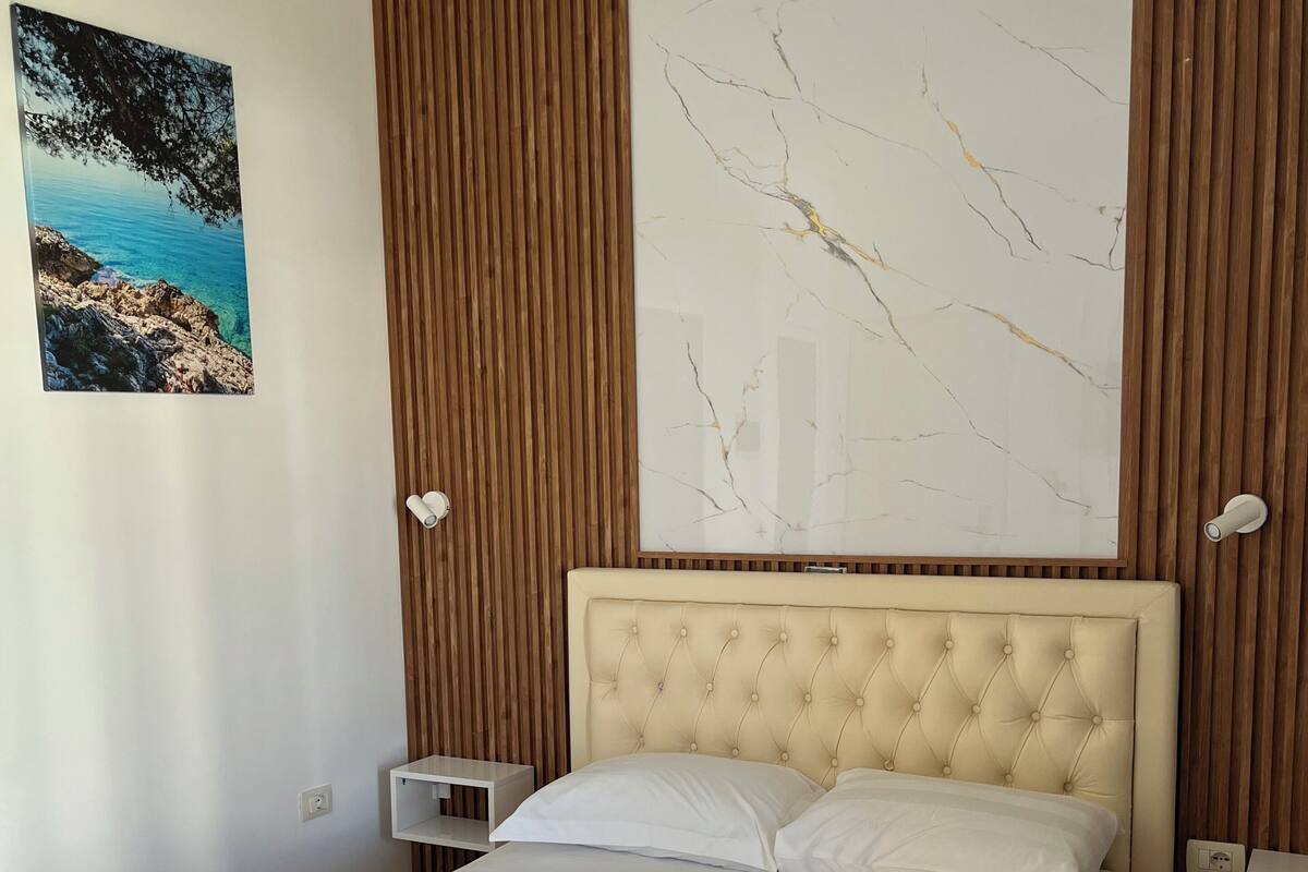 A neatly made bed with white linens and towels, a marble-patterned wall, and a wooden panel wall.