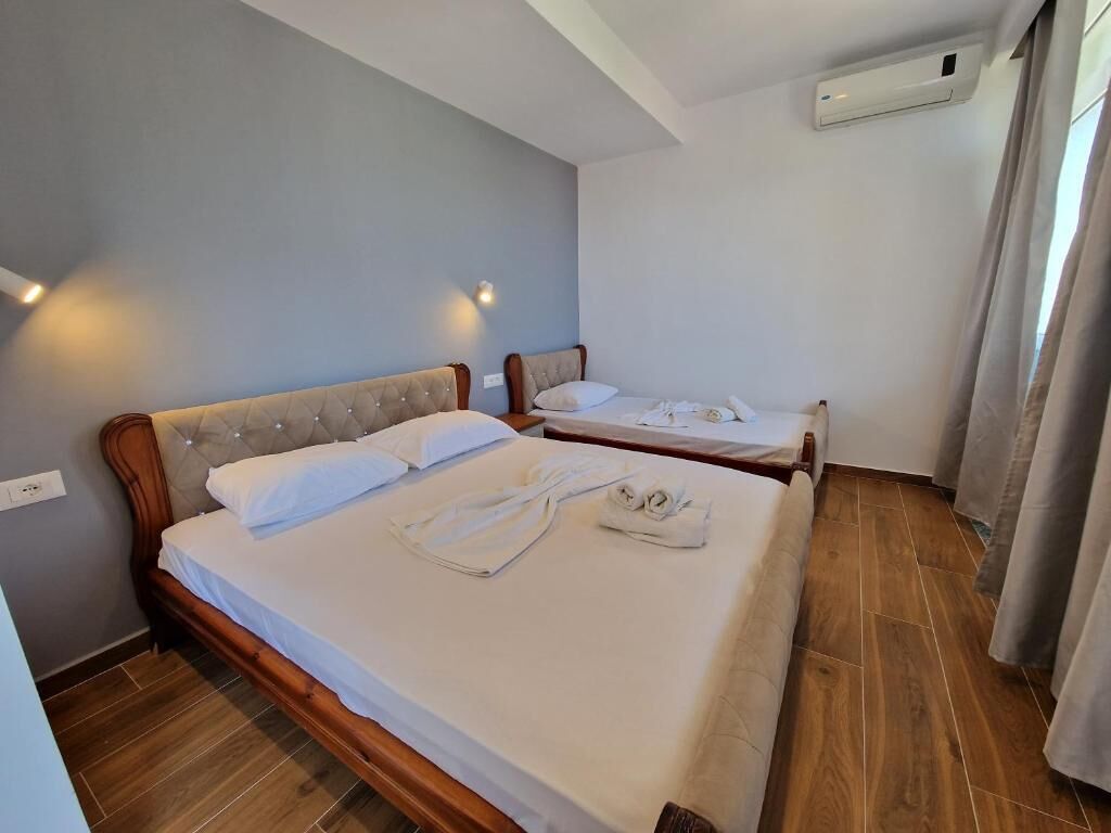 Habitación de hotel con dos camas, piso de madera, pared de color claro y una ventana con cortinas.