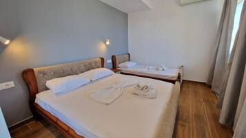 Habitación de hotel con dos camas, piso de madera, pared de color claro y una ventana con cortinas.