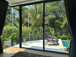 A modern room with a large sliding glass door leading to a private outdoor area with a pool and lounge chairs. - Spacious 4-bedroom villa Naiton beach Phuket (Tambon Sa Khu)