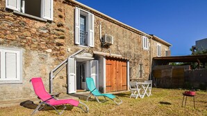 A stone building with a wooden door, a small table with chairs, and a pink and blue lounge chair. - 1 bedroom amazing apartment in Moriani-Plage (Moriani-Plage)