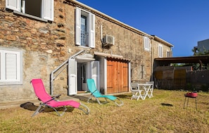 A stone building with a wooden door, a small table with chairs, and a pink and blue lounge chair. - 1 bedroom amazing apartment in Moriani-Plage (Moriani-Plage)