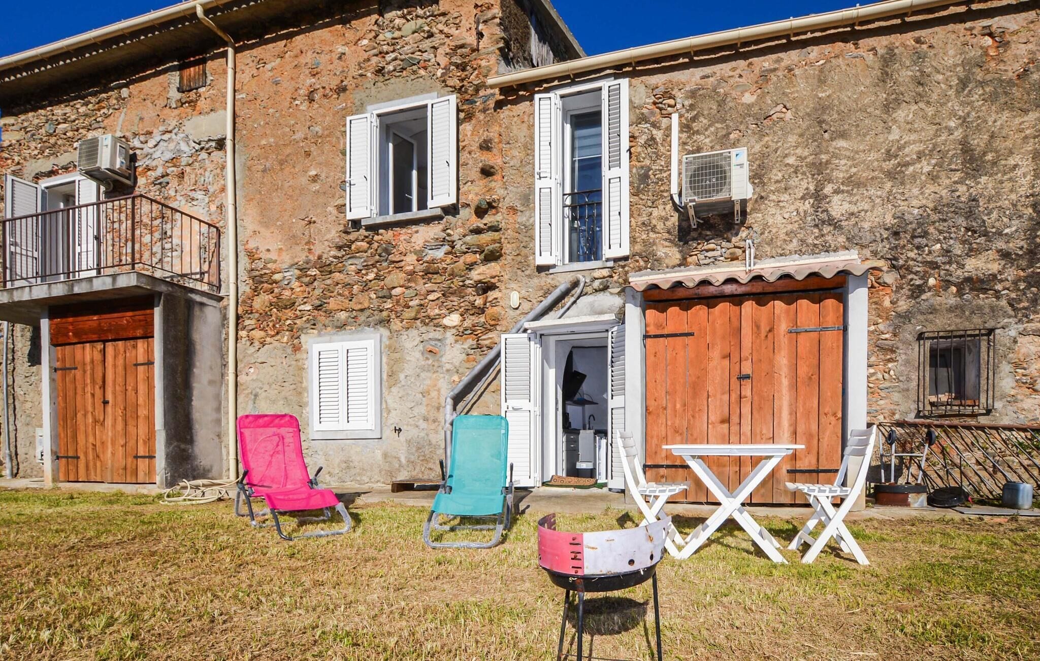A stone building with a balcony, a wooden door, and a small table with chairs.