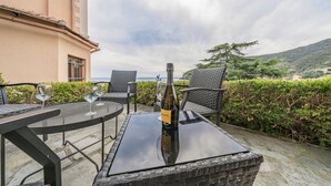 Een terras buiten met rieten meubels, een fles wijn en uitzicht op zee.