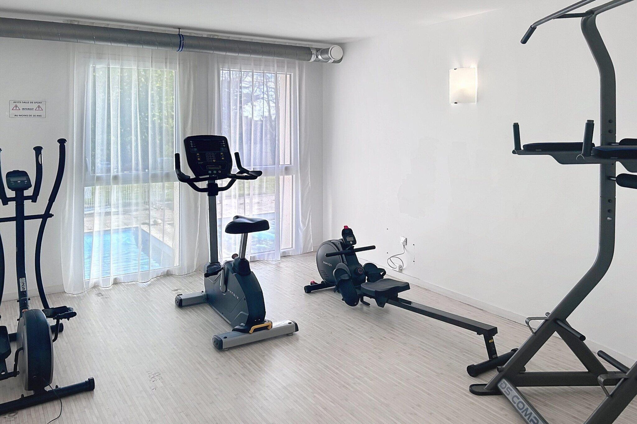 A gym with exercise equipment, a large window with curtains, and a wall-mounted light fixture.