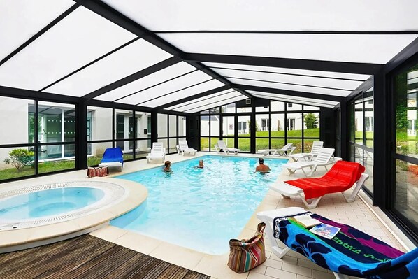 Una piscina con techo de cristal, sillas de descanso y un jacuzzi.