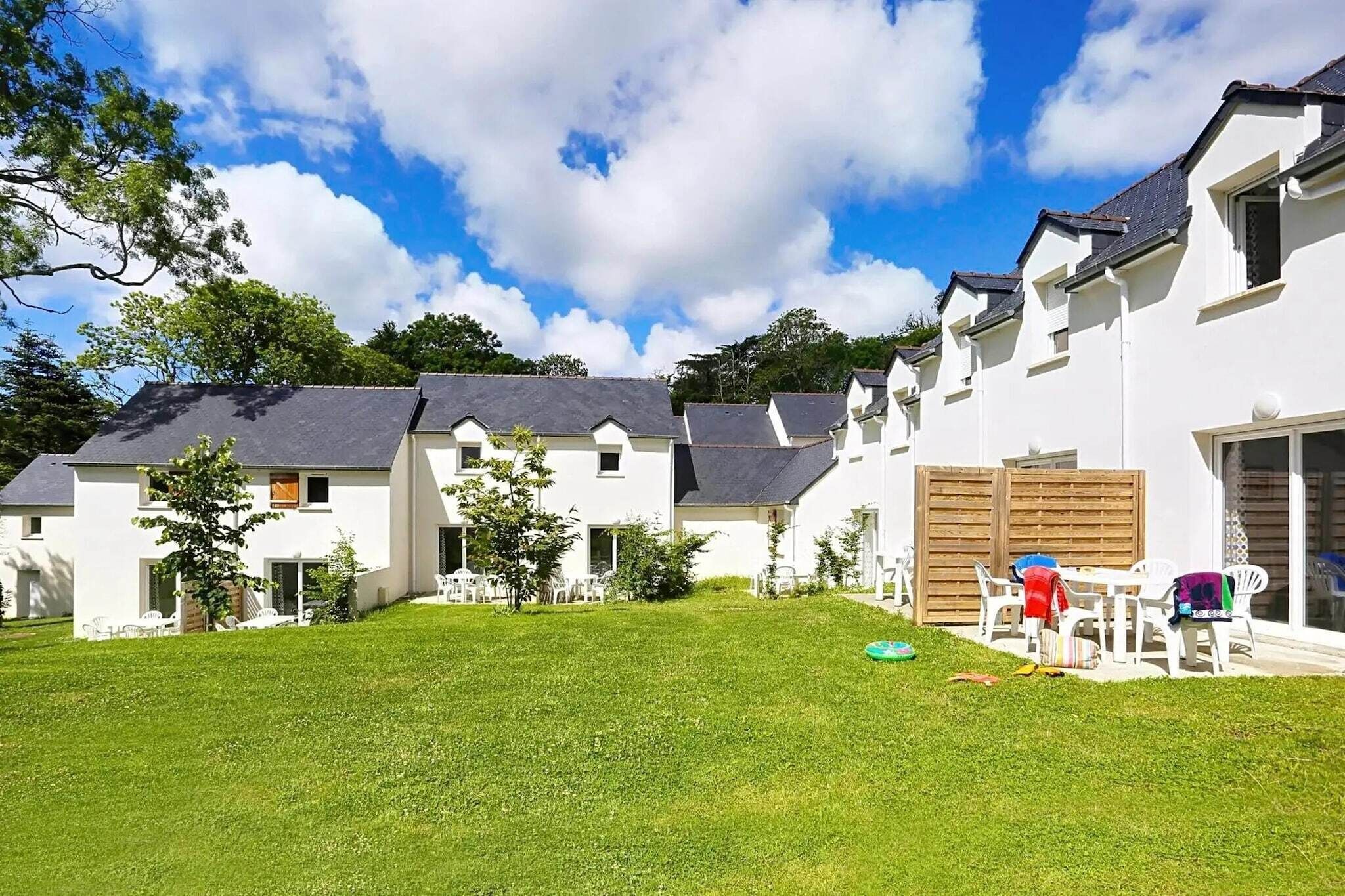A row of white houses with grey roofs, a grassy yard, and a clear blue sky.
