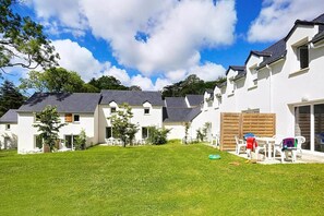 A row of white houses with grey roofs, a grassy yard, and a clear blue sky.